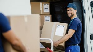 young-happy-manual-worker-carrying-cardboard-boxes-in-delivery-van-while-communicating-with-his-colleagues-1